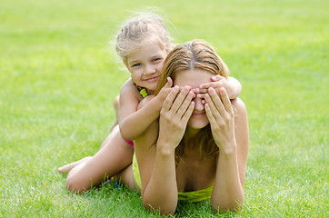 Image showing The daughter of fun mom closed her eyes while lying on a green lawn