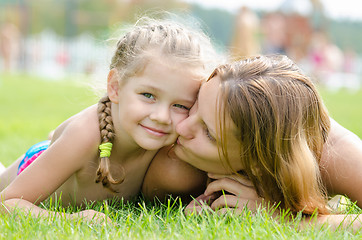 Image showing Mother kissing her daughter lying on a green grass lawn