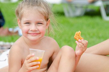 Image showing Girl eats cookies, drinks juice from a plastic disposable cup and smiling looked into the frame