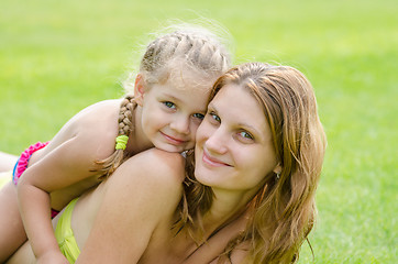 Image showing Daughter lying on mother\'s back happily hugs her, against the background of green grass