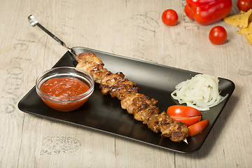 Image showing shashlik. kebab skewer, black rectangular plate. sauce and onions