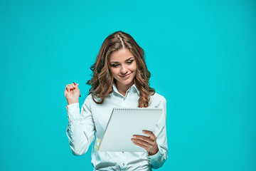 Image showing The smiling young business woman with pen and tablet for notes on blue background