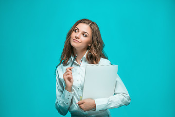 Image showing The smiling young business woman with pen and tablet for notes on blue background