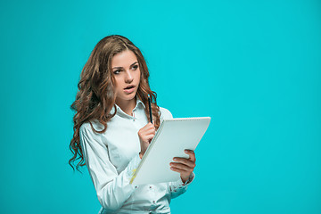 Image showing The thoughtful young business woman with pen and tablet for notes on blue background