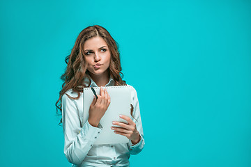 Image showing The thoughtful young business woman with pen and tablet for notes on blue background