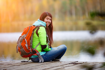 Image showing Smiling brunette sitting with backpack on bridge