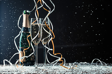 Image showing Champagne bottle, glasses on table covered snow and cascading ribbons