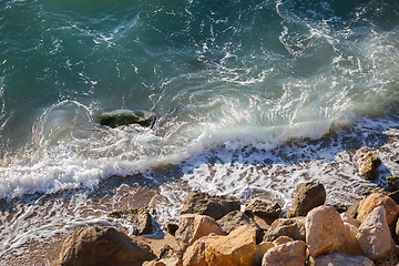 Image showing Small waves, sea foam and coastal rocks on sunny day