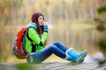 Image showing Young brunette drinking water from bottle at pond