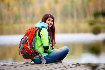 Image showing Cheerful brunette sitting with backpack at lake