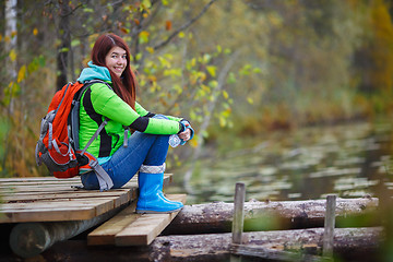 Image showing Young brunette with backpack sitting on bridge by pond