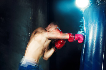 Image showing Male boxer boxing in punching bag with dramatic edgy lighting in a dark studio