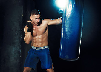 Image showing Male boxer boxing in punching bag with dramatic edgy lighting in a dark studio