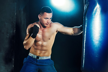 Image showing Male boxer boxing in punching bag with dramatic edgy lighting in a dark studio