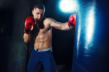 Image showing Male boxer boxing in punching bag with dramatic edgy lighting in a dark studio