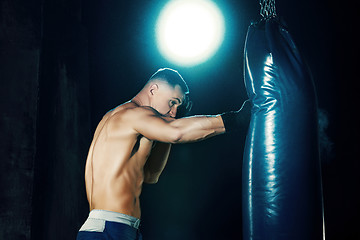 Image showing Male boxer boxing in punching bag with dramatic edgy lighting in a dark studio