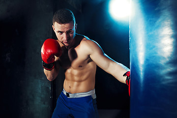 Image showing Male boxer boxing in punching bag with dramatic edgy lighting in a dark studio