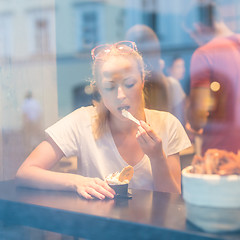 Image showing Young pretty woman eating icecream in gelateria.