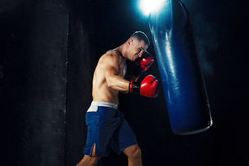 Image showing Male boxer boxing in punching bag with dramatic edgy lighting in a dark studio