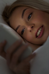 Image showing young woman with smartphone in bed at night