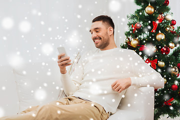 Image showing smiling man with smartphone at home for christmas