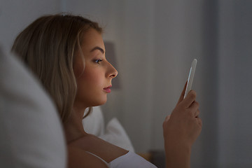 Image showing young woman with smartphone in bed at night