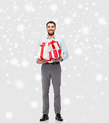 Image showing happy young man holding christmas gifts over snow