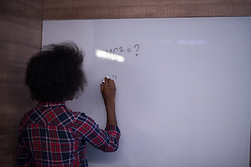 Image showing African American woman writing on a chalkboard in a modern offic