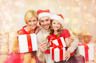 Image showing smiling family holding gift boxes and sparkles