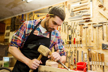 Image showing carpenter with wood, hammer and chisel at workshop