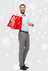 Image showing smiling man with red shopping bags over snow