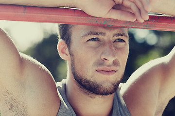 Image showing young man exercising on horizontal bar outdoors