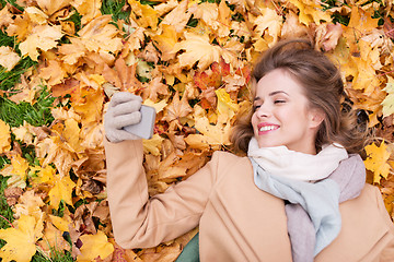 Image showing woman on autumn leaves taking selfie by smartphone