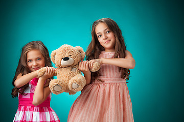 Image showing The two cute little girls on blue background with Teddy bear