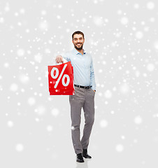 Image showing smiling man with red shopping bag over snow