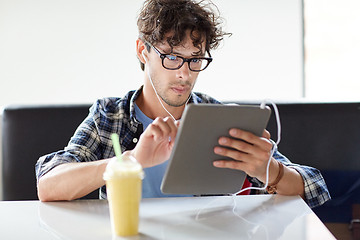 Image showing man with tablet pc and earphones sitting at cafe