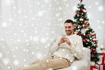 Image showing smiling man with smartphone at home for christmas