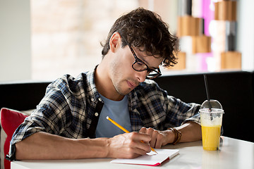 Image showing man with notebook and juice writing at cafe