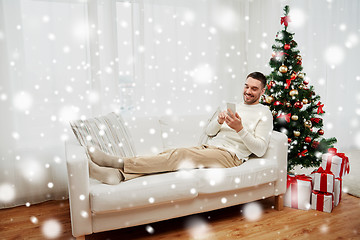 Image showing smiling man with smartphone at home for christmas