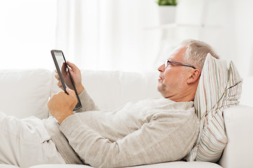 Image showing senior man with tablet pc lying on sofa at home