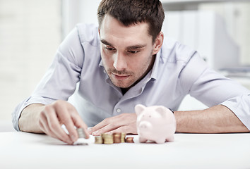 Image showing businessman with piggy bank and coins at office