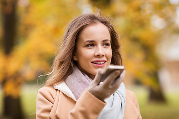 Image showing woman recording voice on smartphone in autumn park