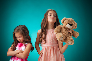 Image showing The two cute little girls on blue background with Teddy bear