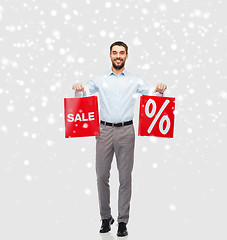 Image showing smiling man with red shopping bags over snow