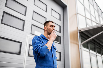 Image showing auto mechanic smoking cigarette at car workshop