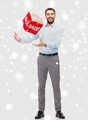 Image showing smiling man playing with red sale sign over snow