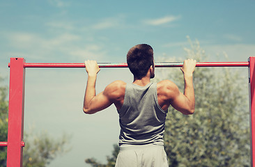 Image showing young man exercising on horizontal bar outdoors