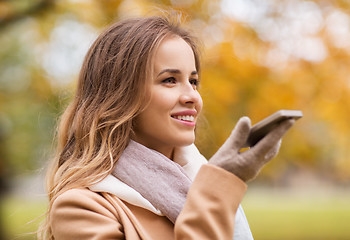 Image showing woman recording voice on smartphone in autumn park