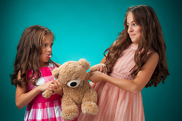 Image showing The two cute little girls on blue background with Teddy bear