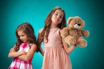 Image showing The two cute little girls on blue background with Teddy bear